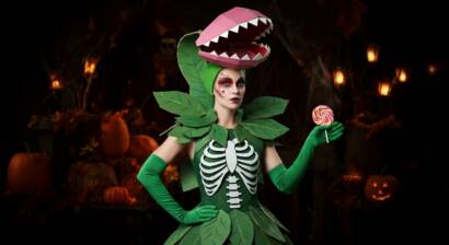 Costume design of Venus Fly Trap Vickie, featuring a vibrant green dress with leaf patterns, long green gloves resembling plant stems, and a headpiece shaped like the open jaws of a Venus flytrap with red and pink inner petals.