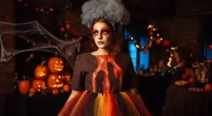 A woman dressed as "Volcano Vickie" at a Halloween party. She wears a dark brown dress resembling a volcano, with a large black fabric volcano structure at her waist. Bright red, orange, and yellow tulle flows down from the volcano, mimicking lava.